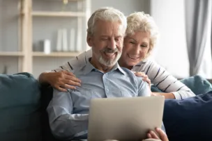 Um casal de idosos sorrindo e olhando para a tela do computador